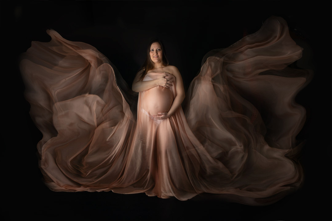 Servizio fotografico gravidanza donna con velo svolazzante fondale nero