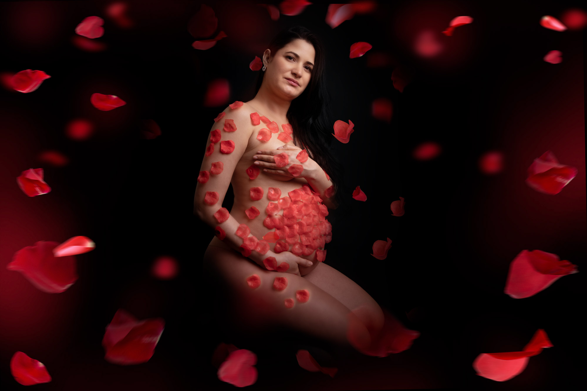 servizio fotografico gravidanza con petali rossi su fondale nero